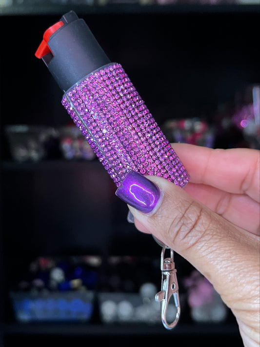 Purple blinged-out pepper spray with a keychain held by a hand.